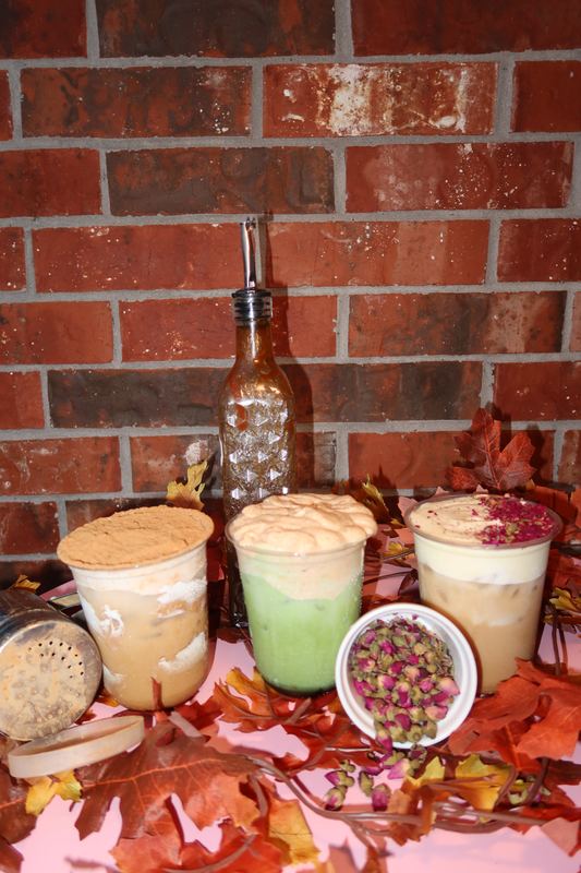 Three iced drinks with a syrup bottle and a bowl of dried rosebuds